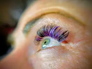 Detailaufnahme einer Wimpernverlängerung mit teilweise lila farbigen Wimpernextensions