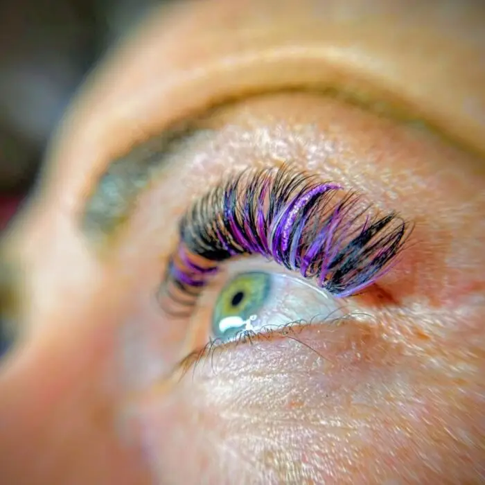 Detailaufnahme einer Wimpernverlängerung mit teilweise lila farbigen Wimpernextensions